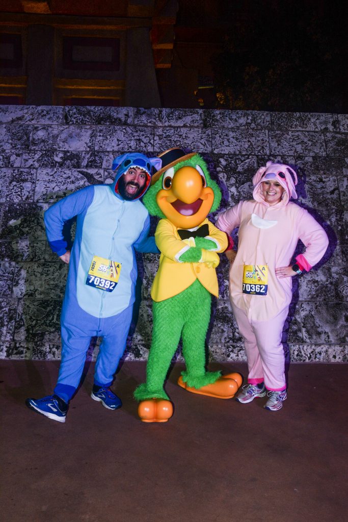 Katie and Spencer in Lilo and Stitch onesies meeting Disney Character Jose Carioca during 2020 Disney World 5K